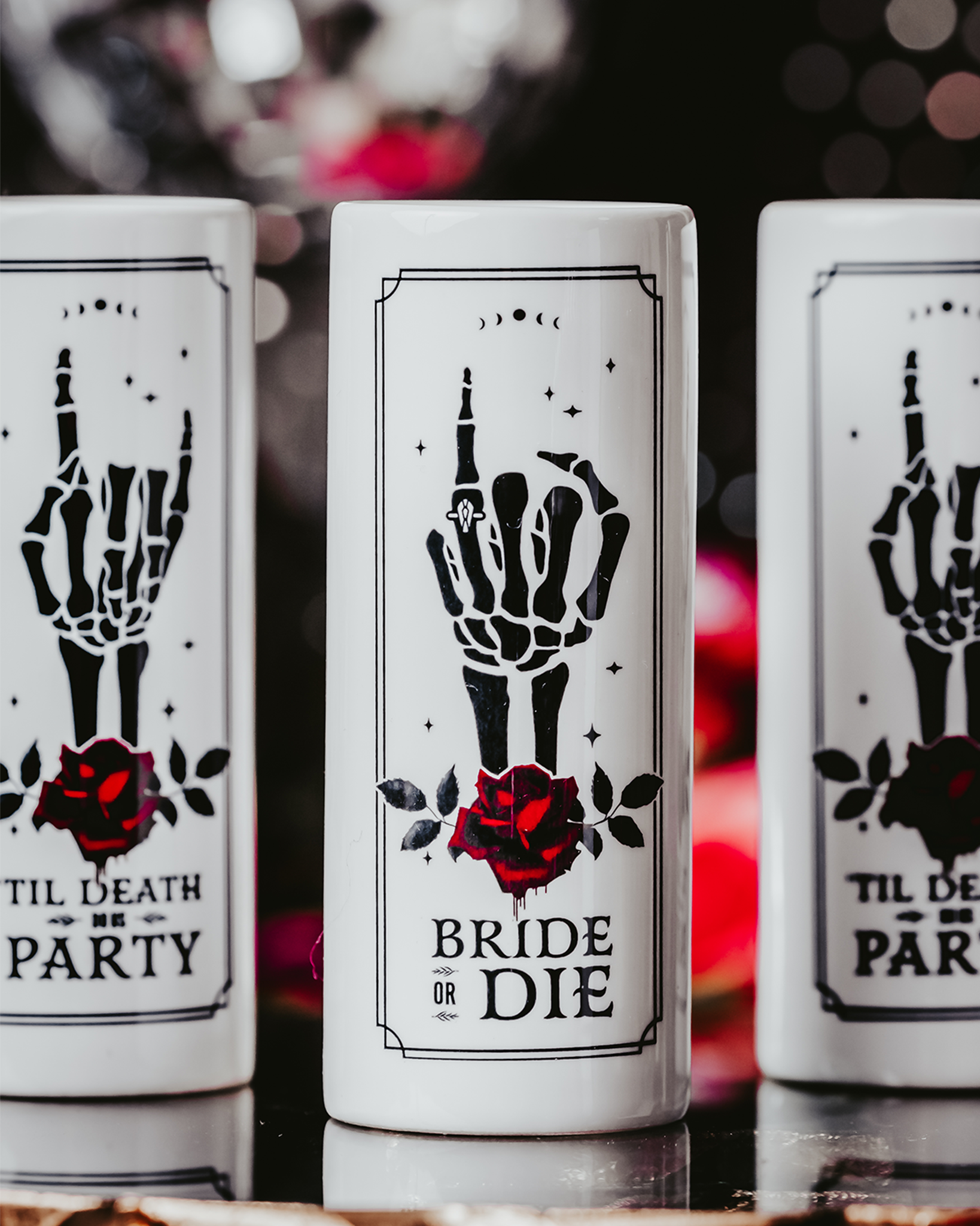 Gothic-style ceramic shot glasses featuring skeleton hand designs with red roses and phrases like "Bride or Die" and "'Til Death Do Us Party," perfect for an alternative bridal party.