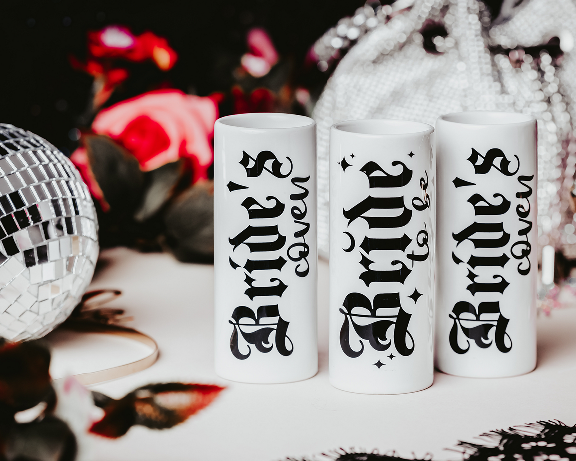 Ceramic shot glasses with gothic-style 'Bride to Be' and 'Bride's Coven' typography, perfect for a non-traditional bride and her bridal party, set against a dark, elegant backdrop.