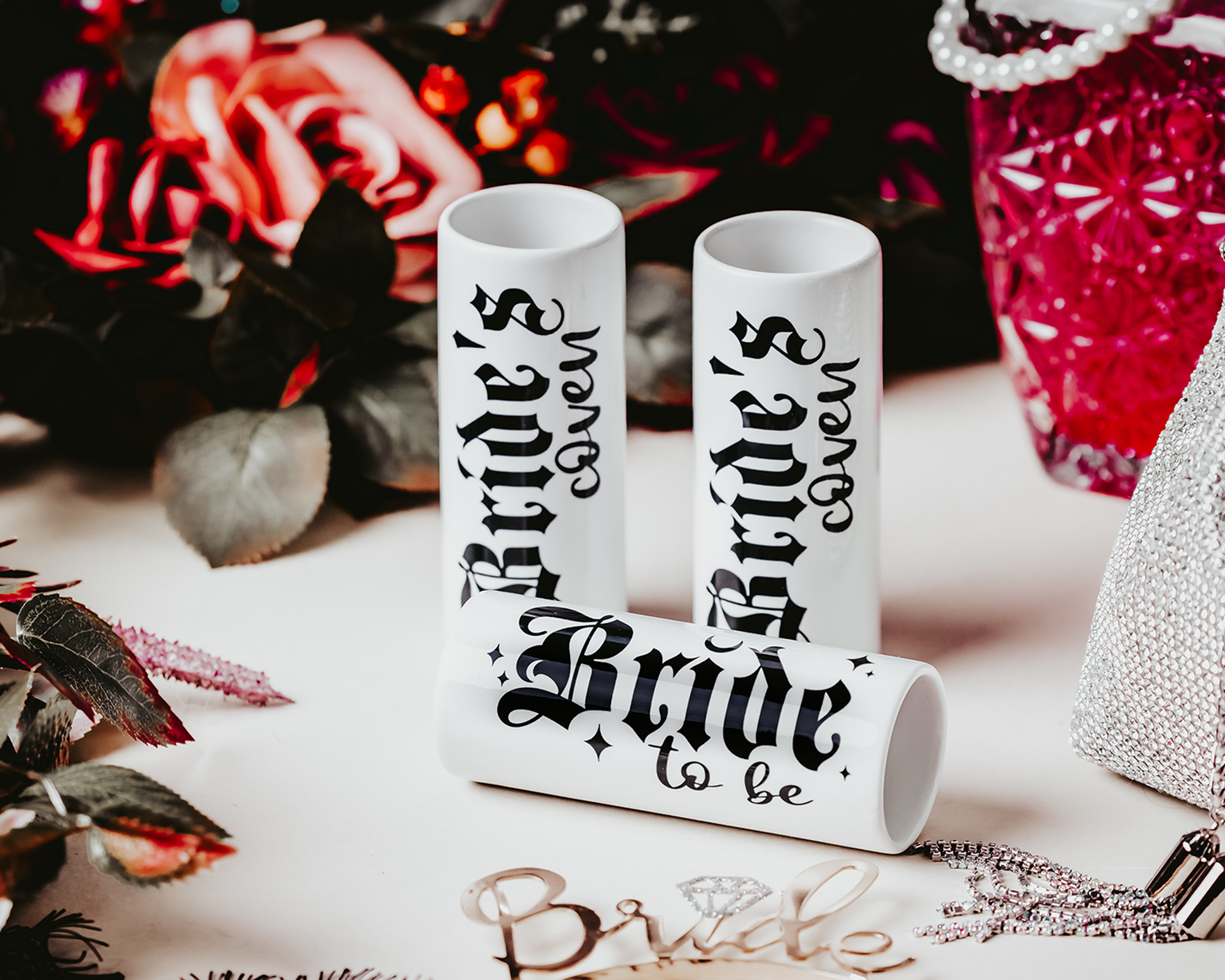 Ceramic shot glasses with gothic-style 'Bride to Be' and 'Bride's Coven' typography, perfect for a non-traditional bride and her bridal party, set against a dark, elegant backdrop.