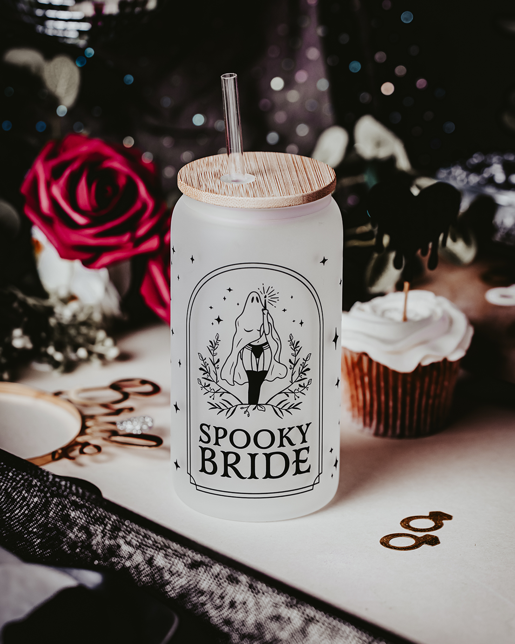 Spooky Bride Frosted Glass Can Tumbler featuring a female ghost design in stockings, with a bamboo lid and clear reusable straw, set against a gothic-themed backdrop with roses and dark décor elements.