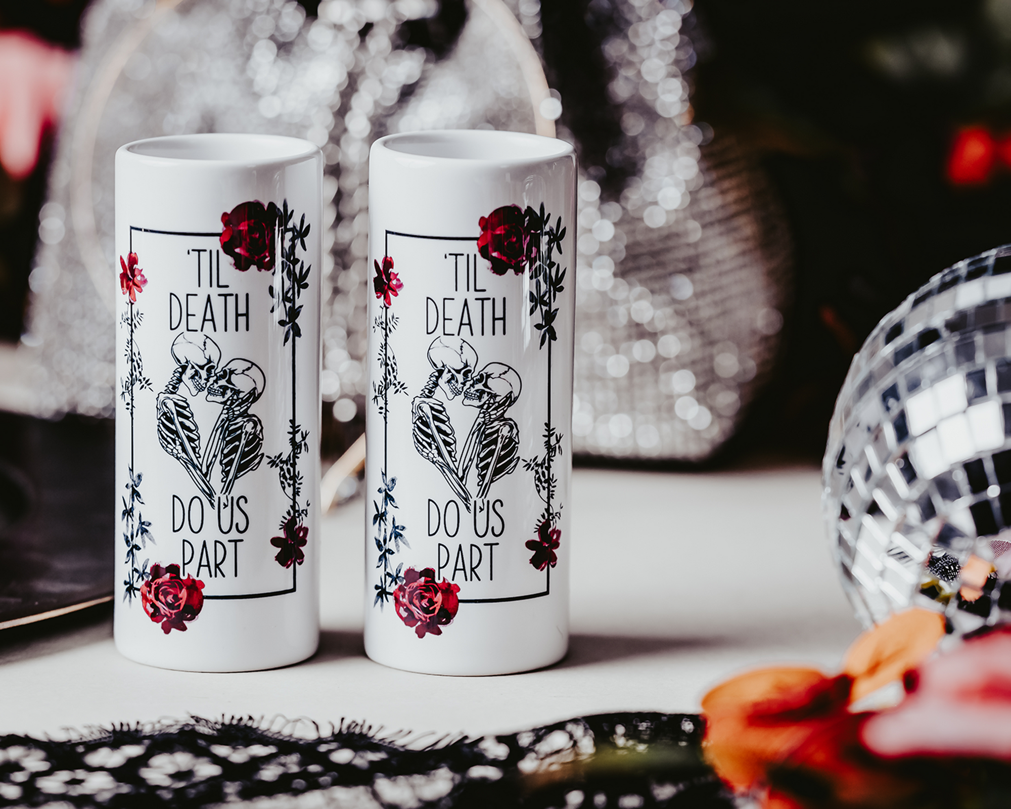 Two white ceramic shot glasses featuring a 'Til Death Do Us Part' skeleton design with red roses, perfect for gothic weddings or bridal gifts. Shot glasses are 3oz and showcase a bold, edgy look.