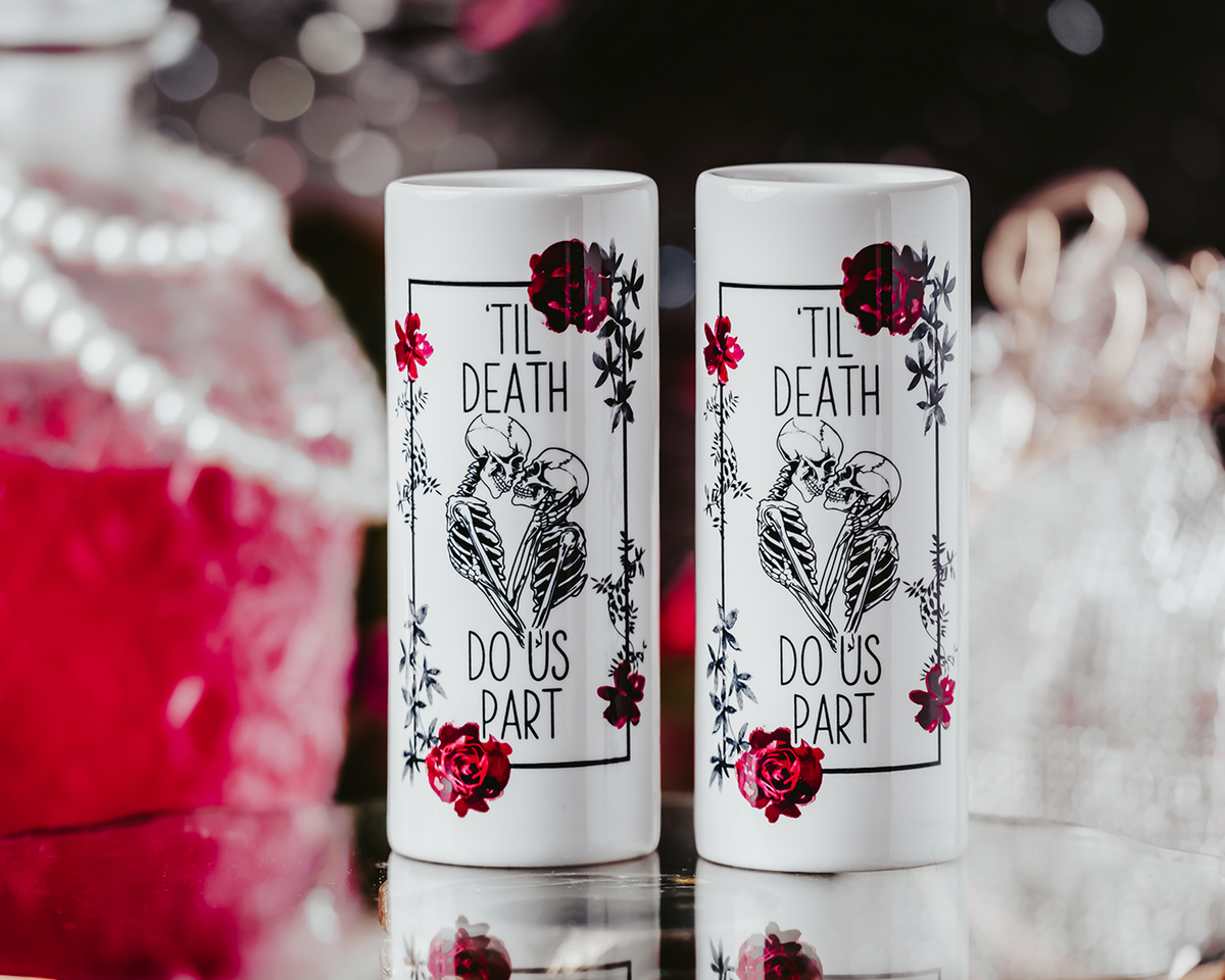 Two white ceramic shot glasses featuring a &#39;Til Death Do Us Part&#39; skeleton design with red roses, perfect for gothic weddings or bridal gifts. Shot glasses are 3oz and showcase a bold, edgy look.